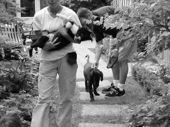 Puppy time out during playtime Young woman holding puppy in arms while young man holds on to his puppy in back garden, as an example of positive dog training.