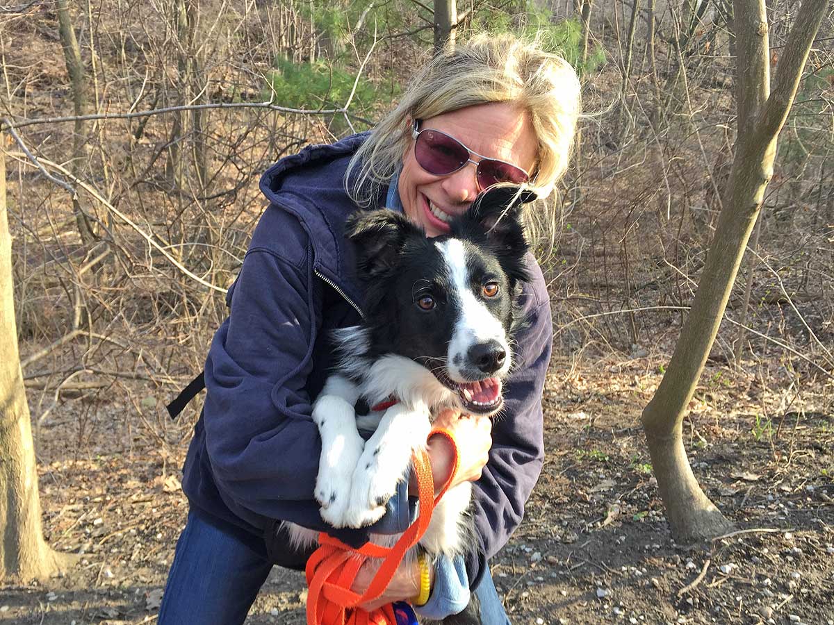 Smiling young woman facing the camera holding her border collie.
